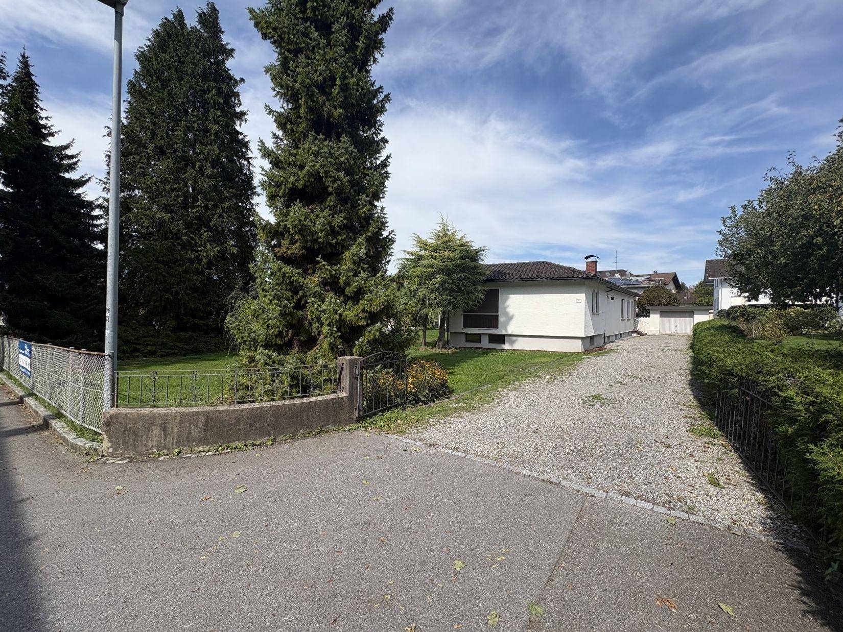 Einfamilienhaus mit großem Vorgarten und Zufahrt, umgeben von hohen Bäumen und viel Grün.