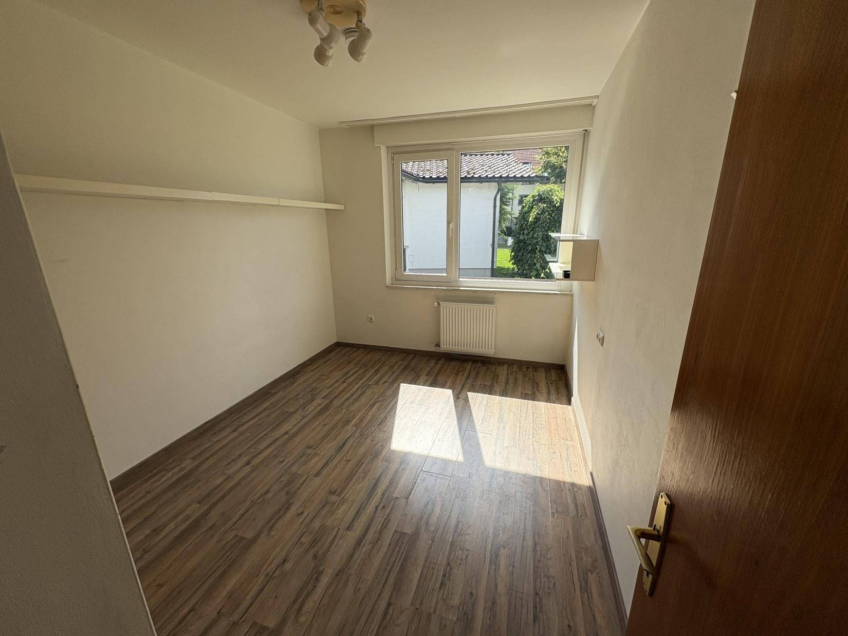 Schlafzimmer mit Laminatboden, weiß gestrichenen Wänden und Fenster zum Garten.