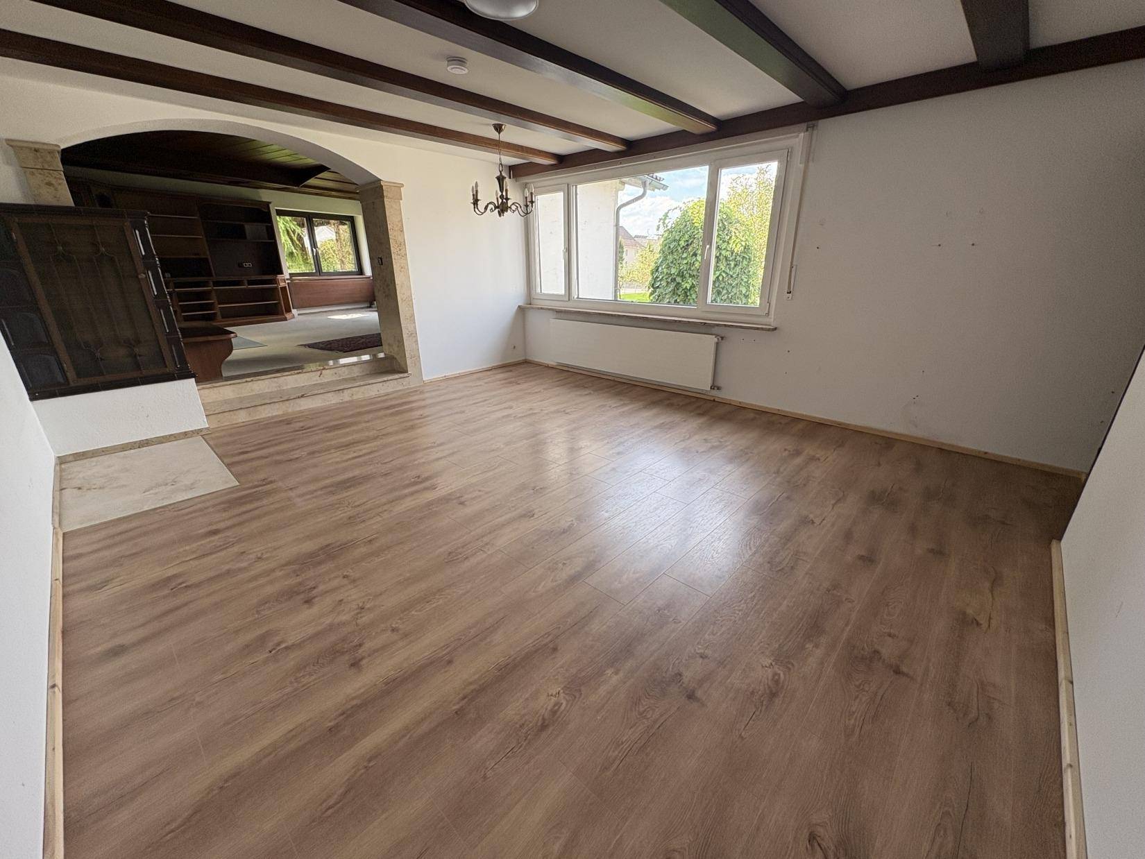 Renoviertes Wohnzimmer mit Laminatboden, Holzbalken und Blick in den Garten.
