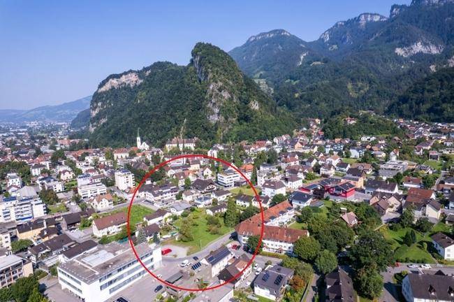 Weitläufige Luftaufnahme einer Stadt mit Bergen im Hintergrund, ein Wohnbereich ist markiert.