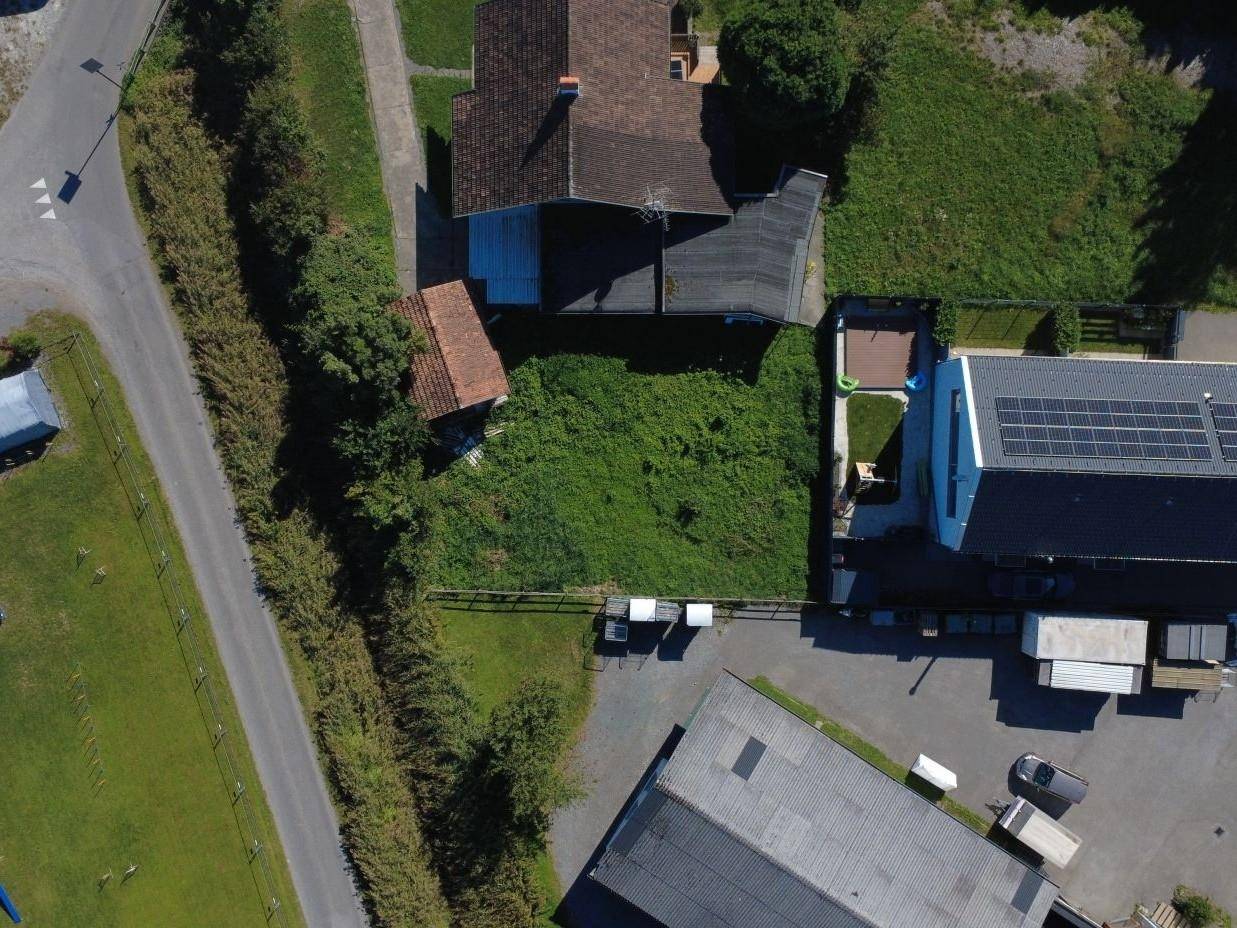 Übersicht aus der Vogelperspektive eines Grundstücks mit gelber Markierung, umgeben von Wohnhäusern und einer Straße.