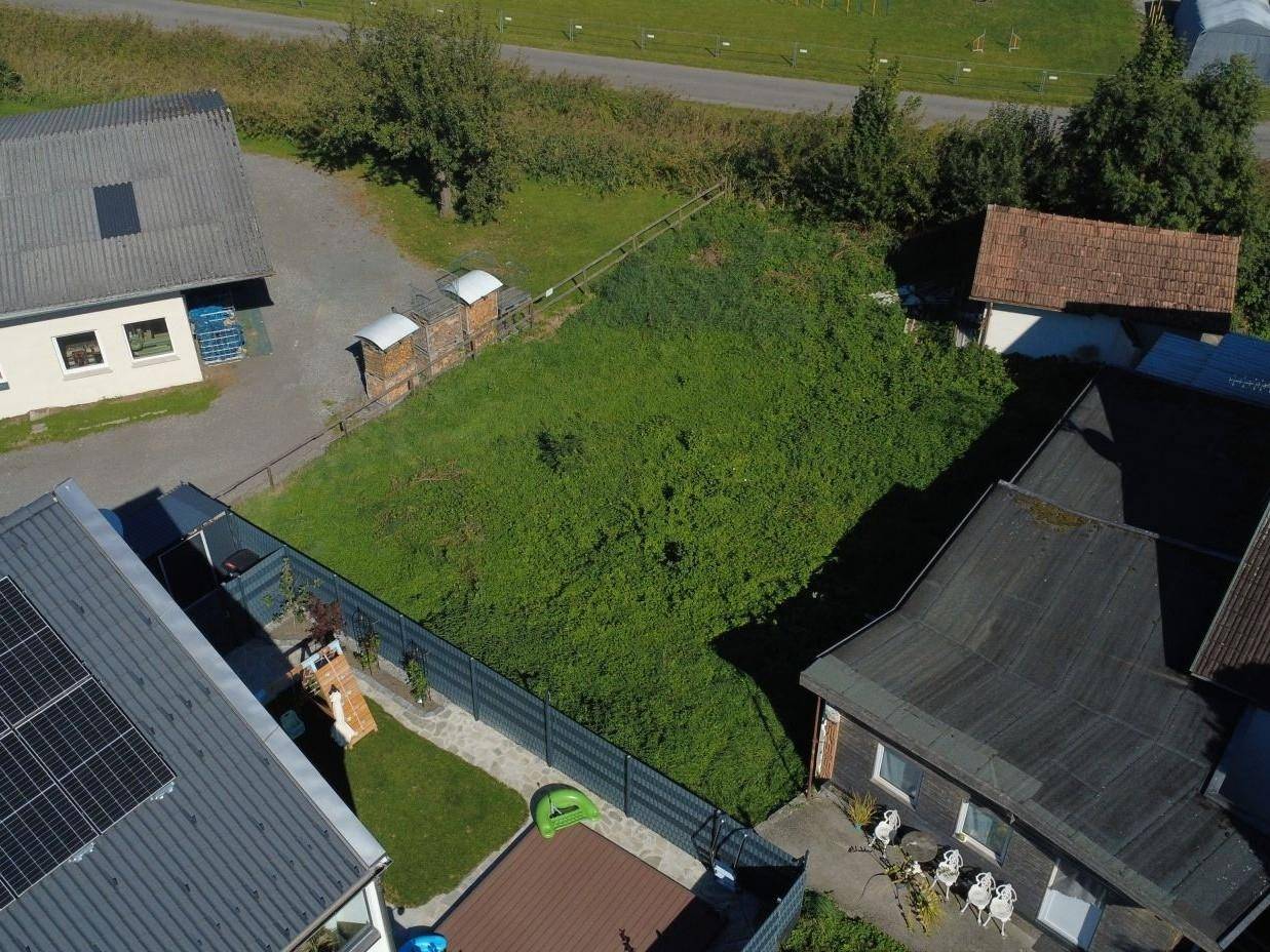 Luftaufnahme eines unbebauten Grundstücks mit dichter Vegetation, umgeben von Zäunen und Häusern mit Solaranlagen.
