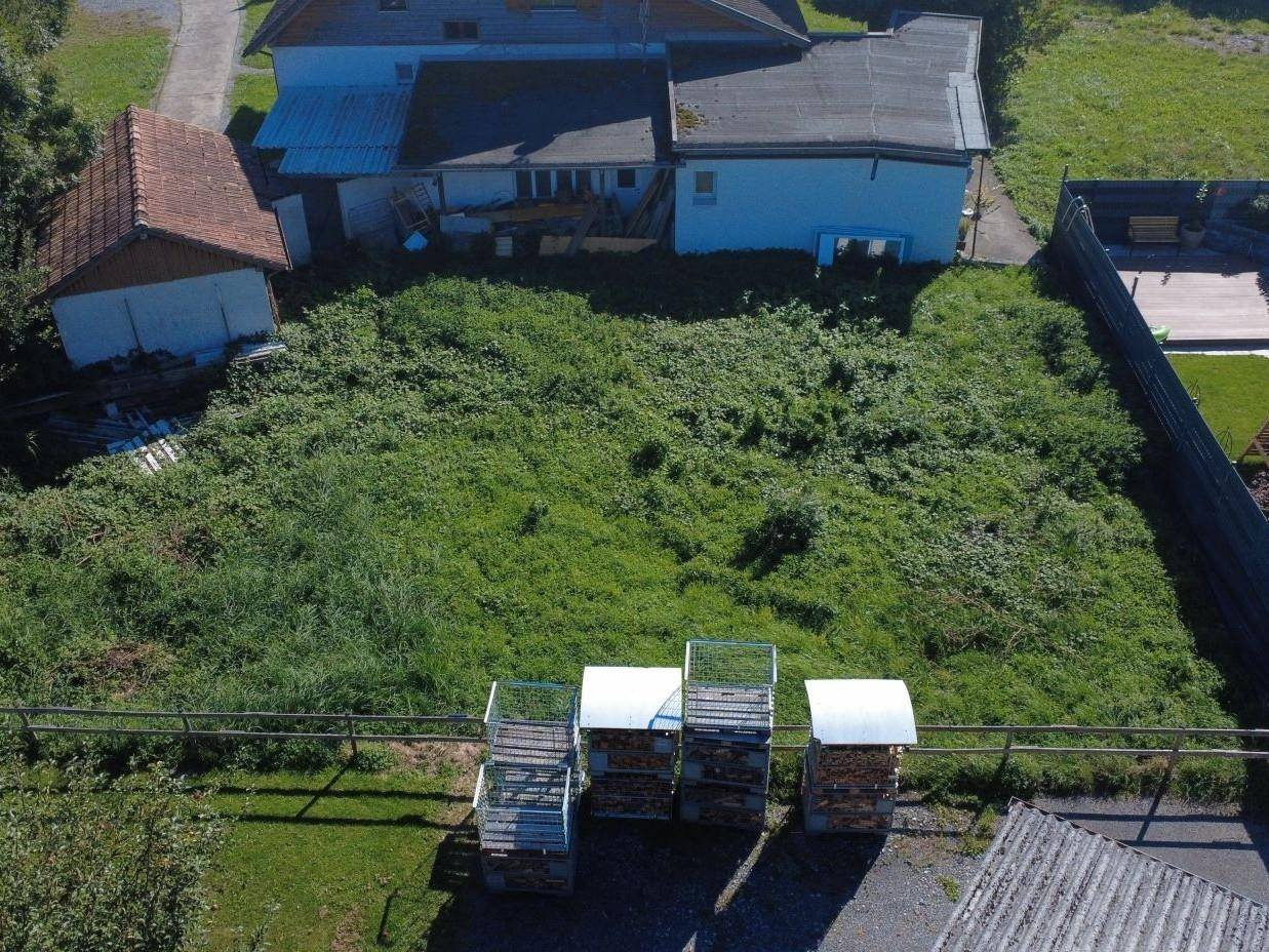 Luftaufnahme eines unbebauten Grundstücks mit üppiger Vegetation, umgeben von Gebäuden und Holzstapeln.