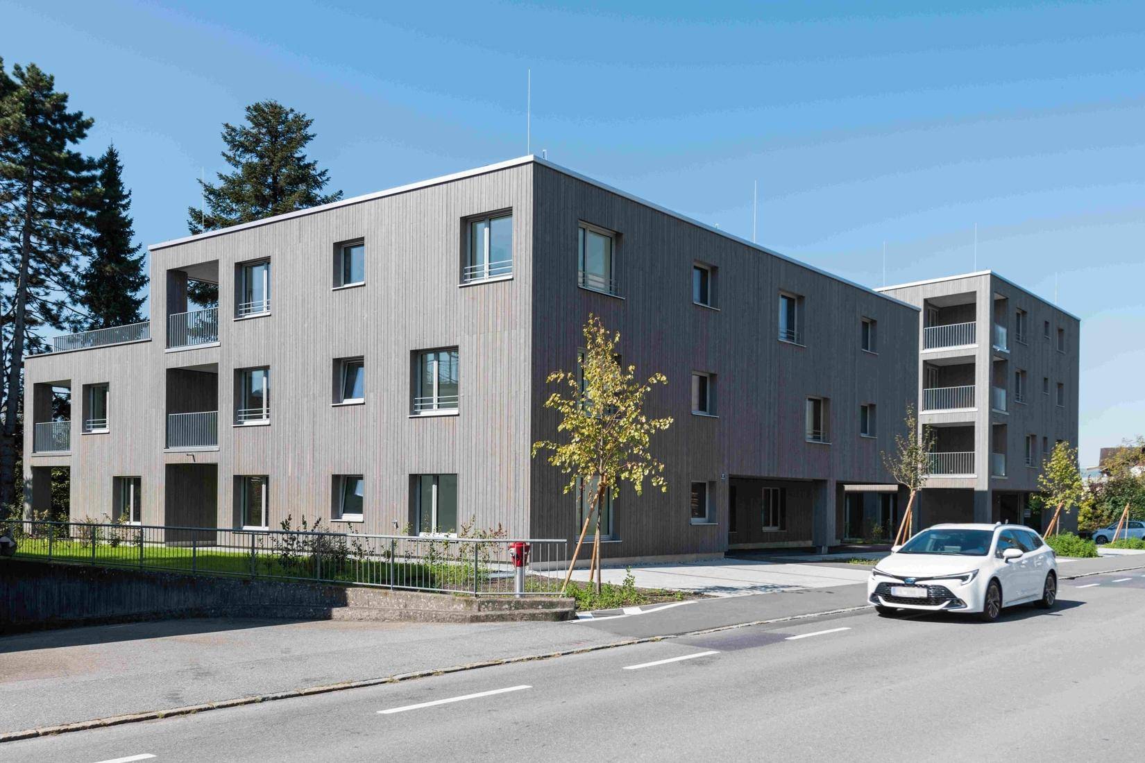 Modernes Mehrfamilienhaus mit Holzfassade und Balkonen an einer ruhigen Wohnstraße.