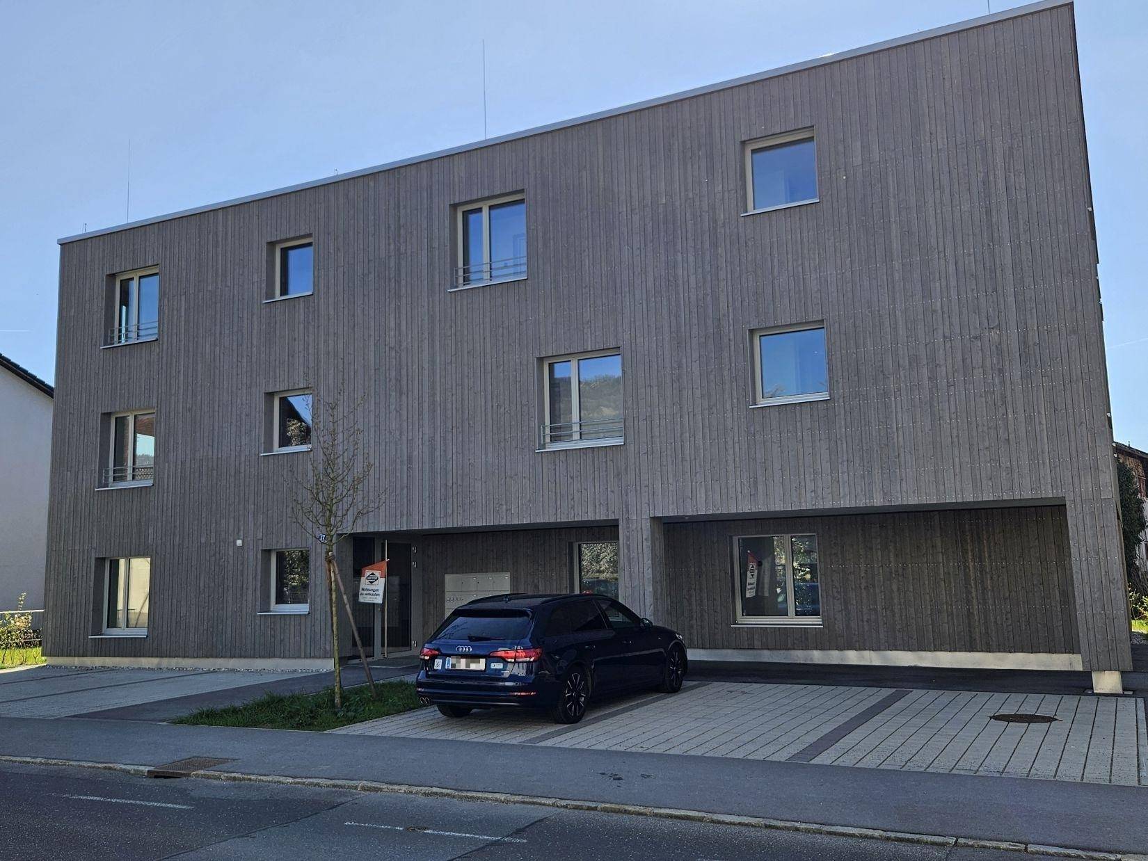 Modernes Wohngebäude mit Holzfassade, Fenstern und Parkplätzen im Freien.