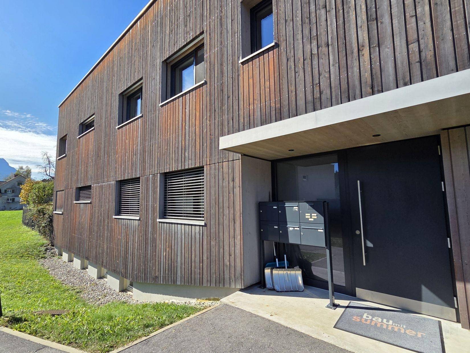 Eingangsbereich eines modernen Wohnhauses mit Holzfassade und Briefkästen.