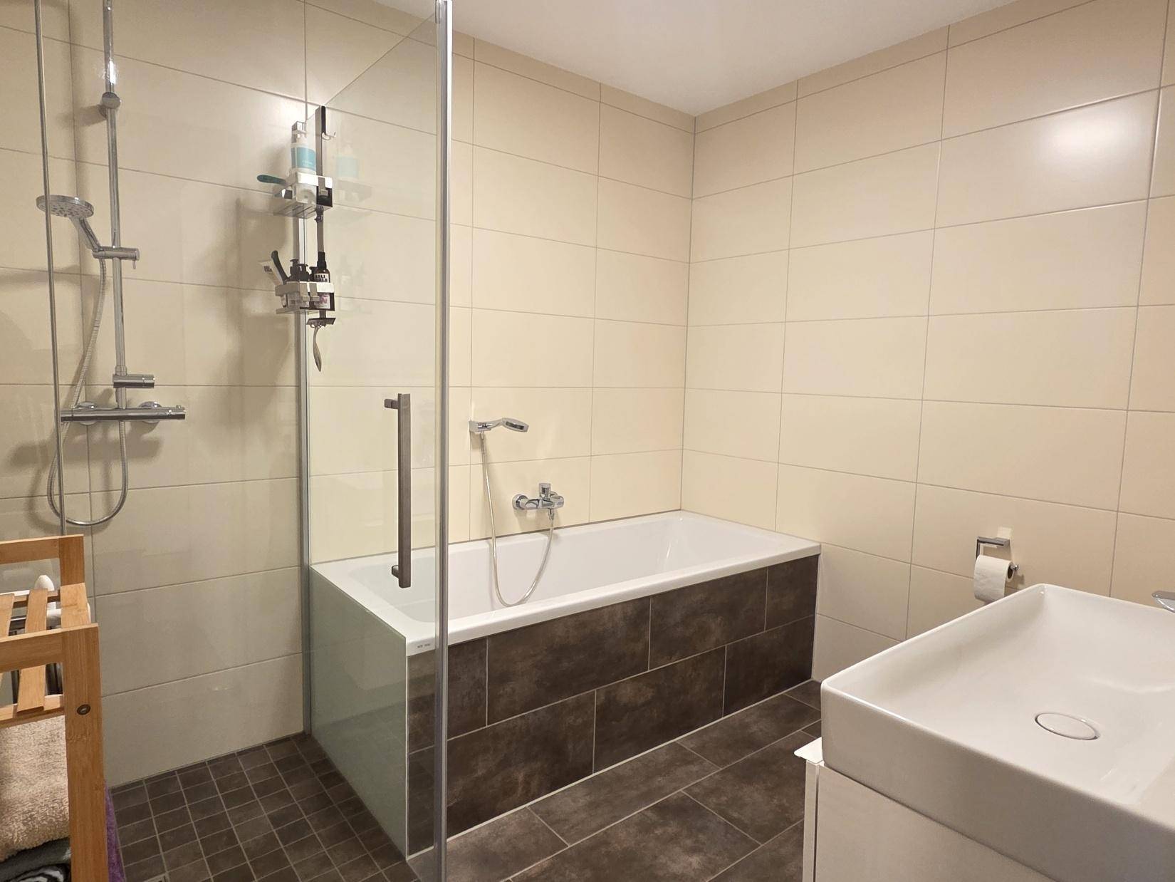 Modernes Badezimmer mit Badewanne, Duschkabine und beigefarbenen Fliesen.