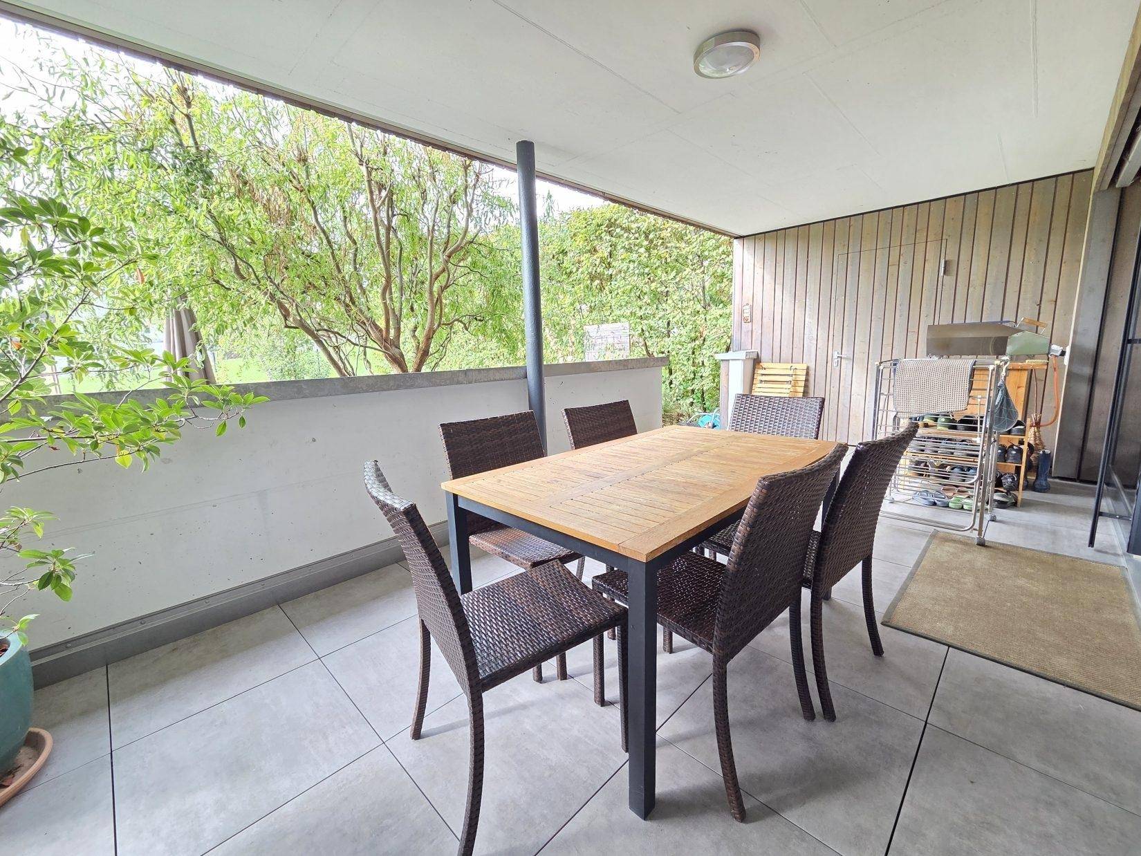 Geräumige, überdachte Terrasse mit Esstisch und Stühlen, umgeben von grüner Vegetation.