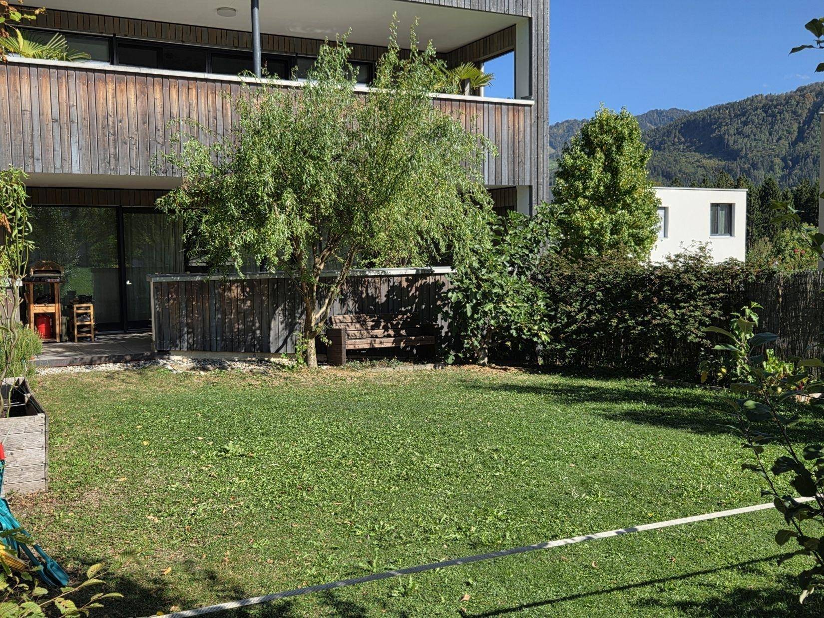 Kleiner, gepflegter Gartenbereich mit Rasenfläche und Sitzbank vor dem Gebäude.