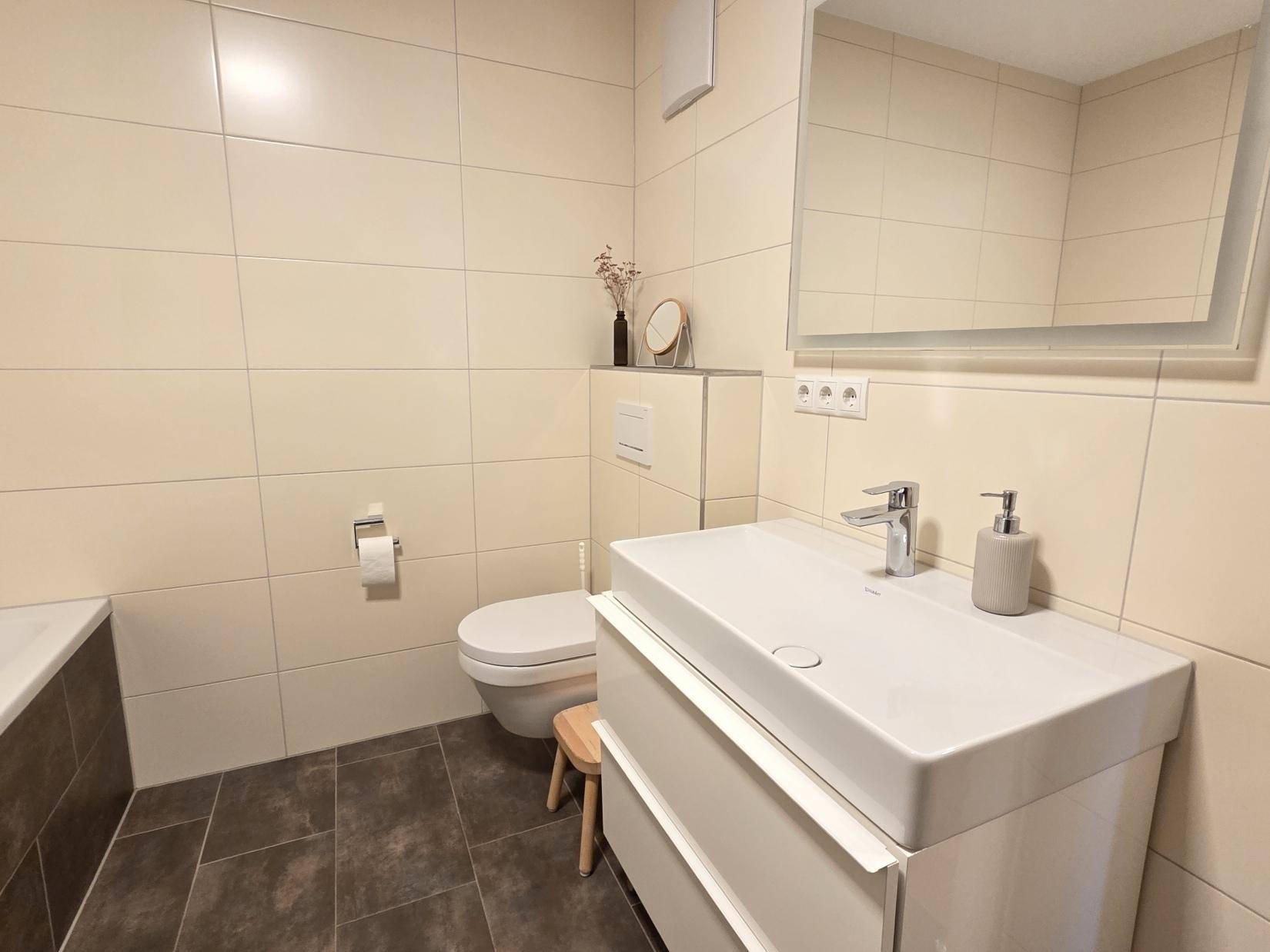 Helles Badezimmer mit WC, Waschbecken und großem Spiegel, modern gefliest.