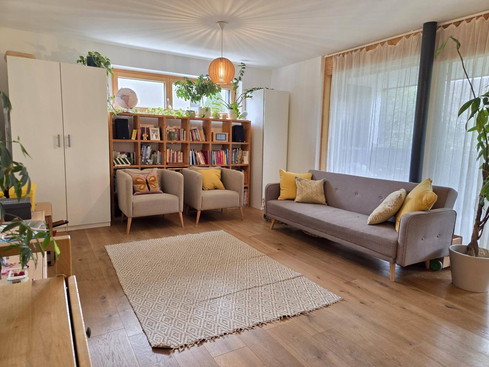 Helles Wohnzimmer mit Holzboden, bequemen Möbeln und vielen Pflanzen, offen gestaltet.