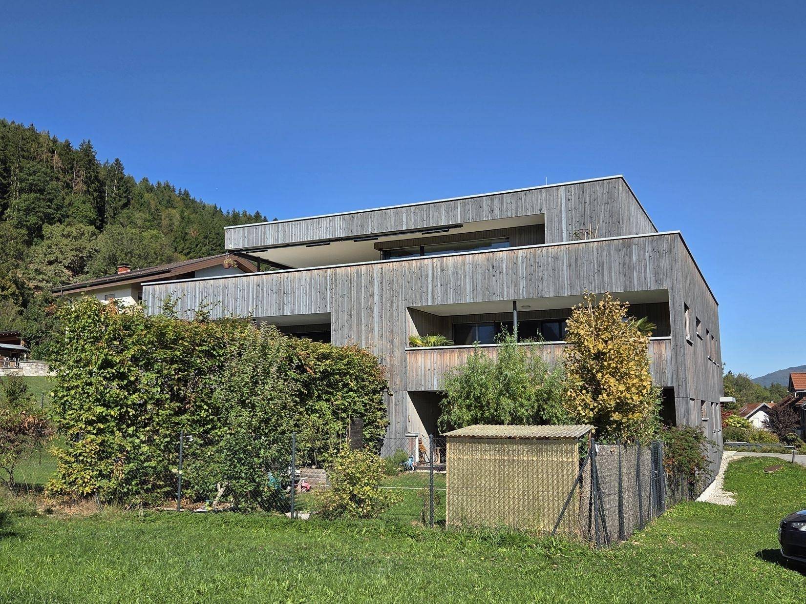 Modernes Wohngebäude mit Holzverkleidung und privatem Gartenbereich in sonniger Lage.
