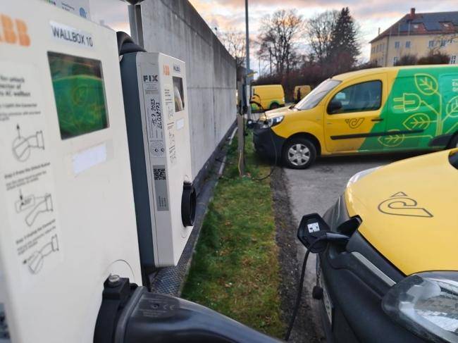 Elektrofahrzeug-Ladestationen an einer Betonwand mit geparkten Lieferwagen.