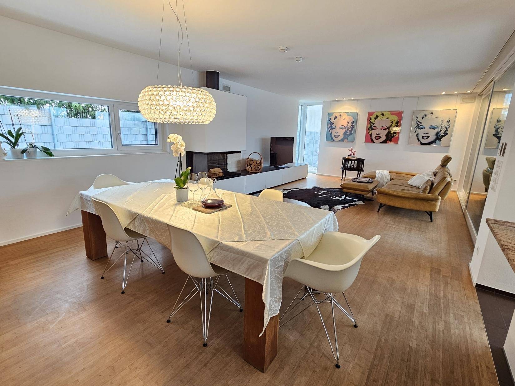 Eleganter Essbereich mit großem Tisch, moderner Hängelampe und Blick zum Wohnzimmer.