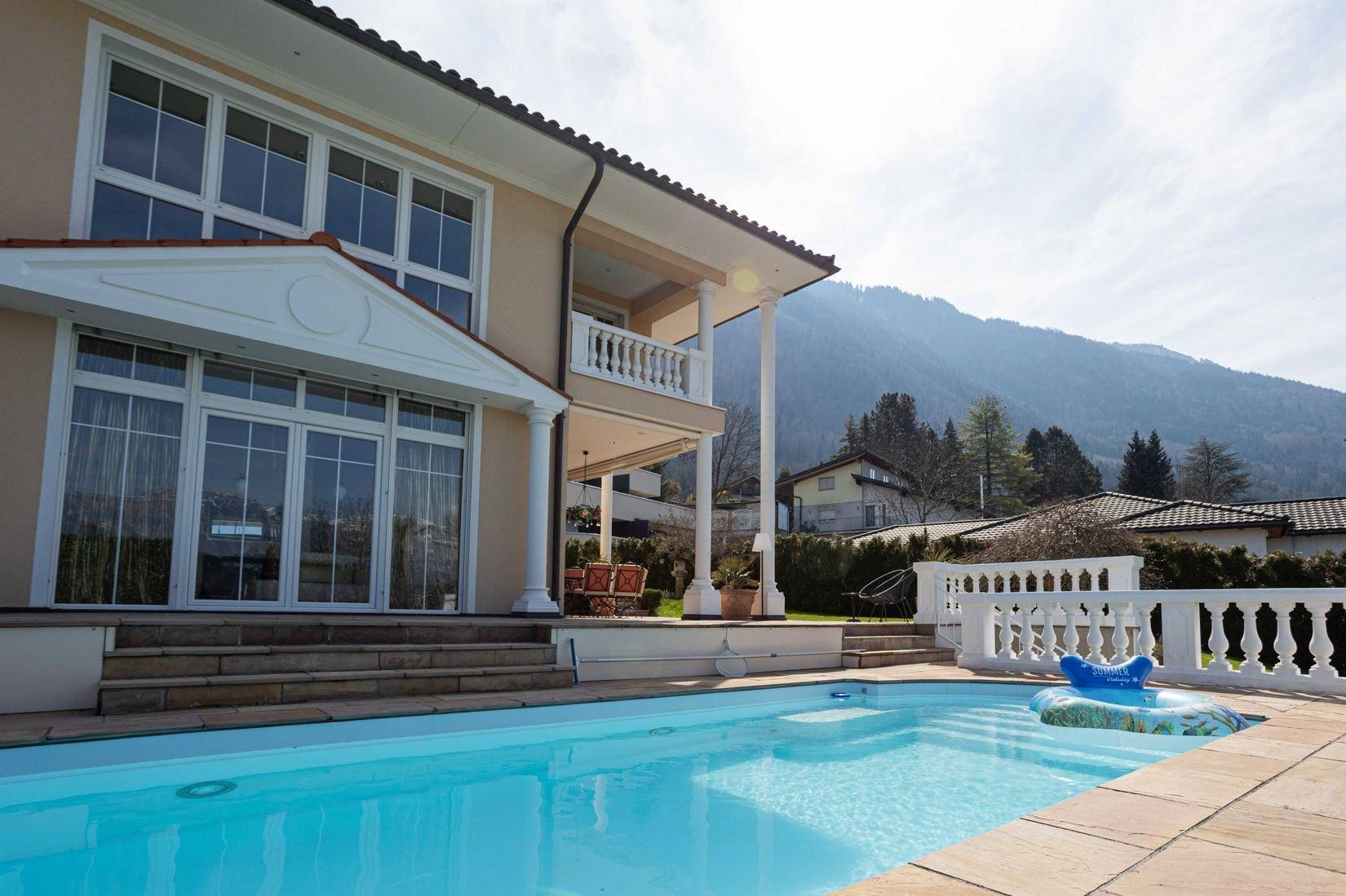 Villa mit großem Pool und Terrasse, umgeben von Bergen und viel Grün.