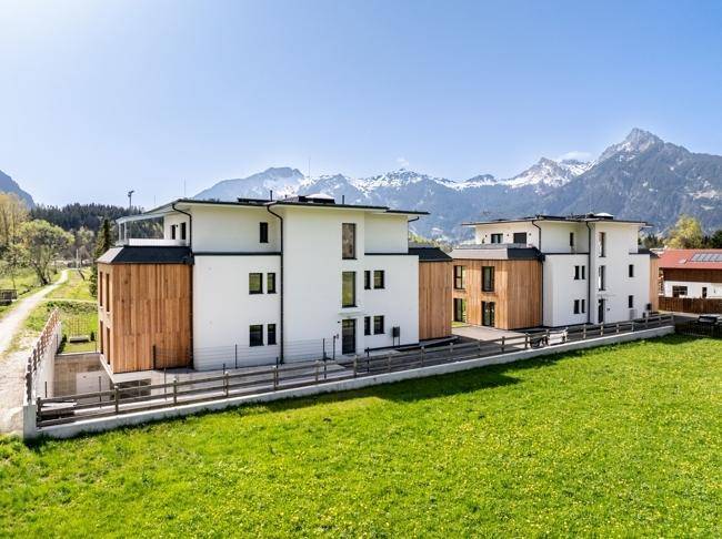 Neubau-Apartments mit moderner Architektur, Holzfassade und Blick auf die schneebedeckten Berge.