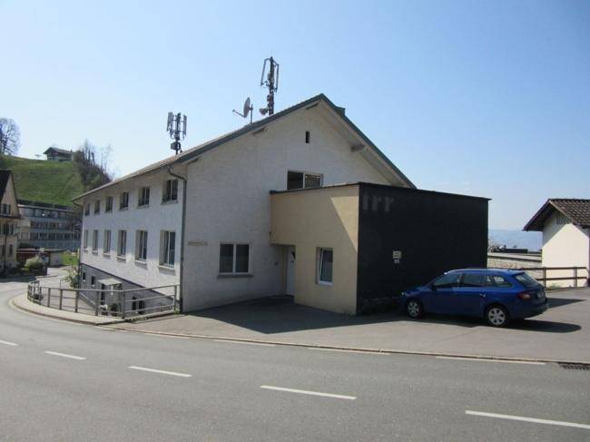 Rückansicht des Gebäudes mit Parkplatz und angrenzendem Anbau unter blauem Himmel.