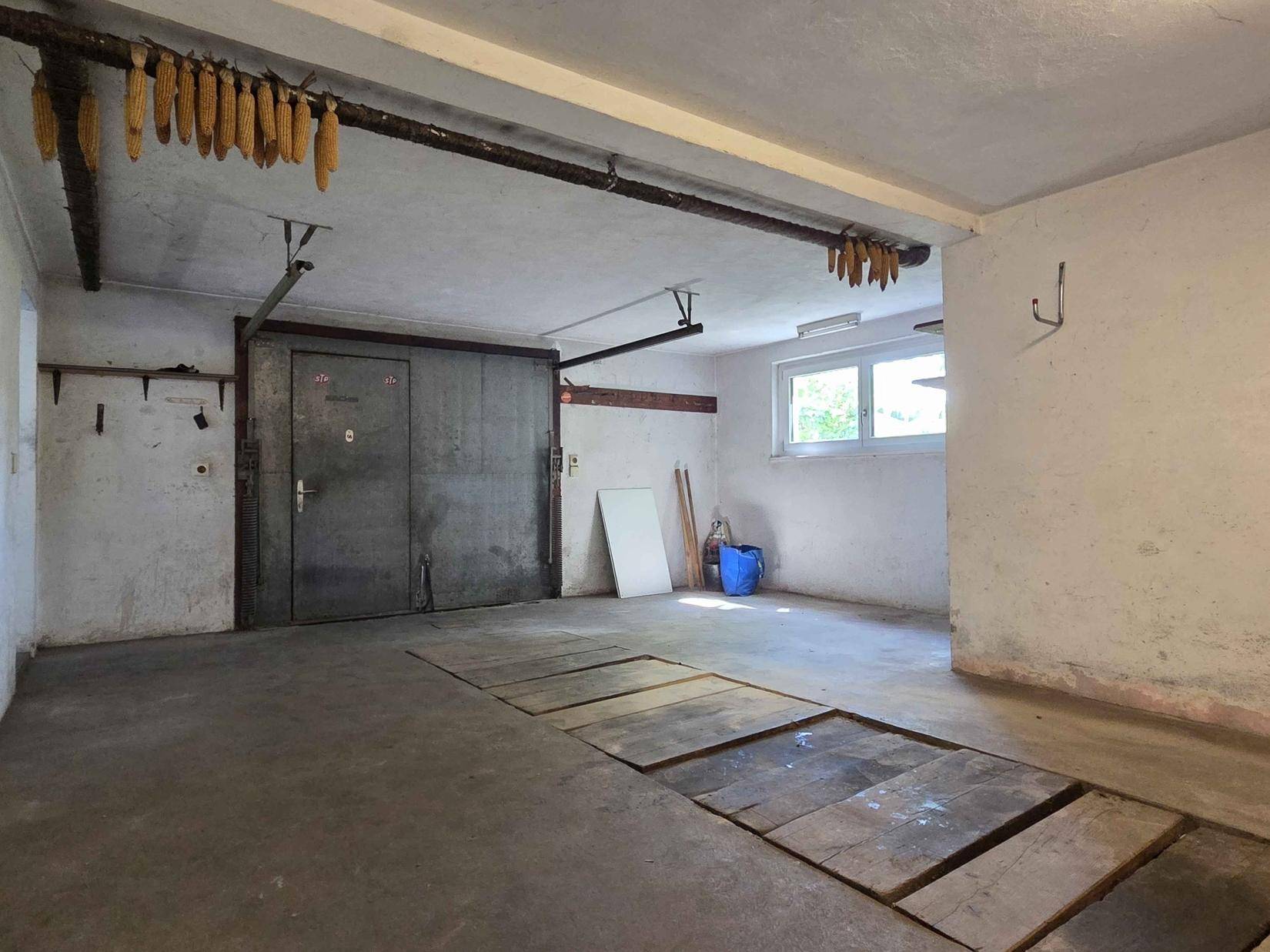 Geräumige Garage oder Lagerraum mit großem Metalltor und Wartungsgrube.