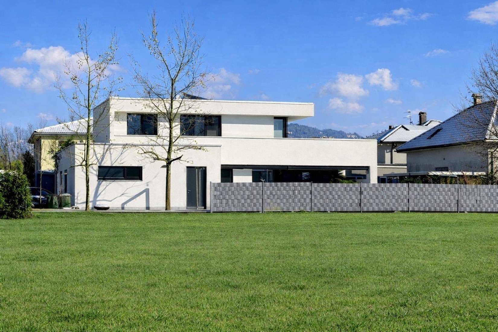 Moderne Villa mit weißer Fassade und großem Rasen, umgeben von einer grünen Landschaft.