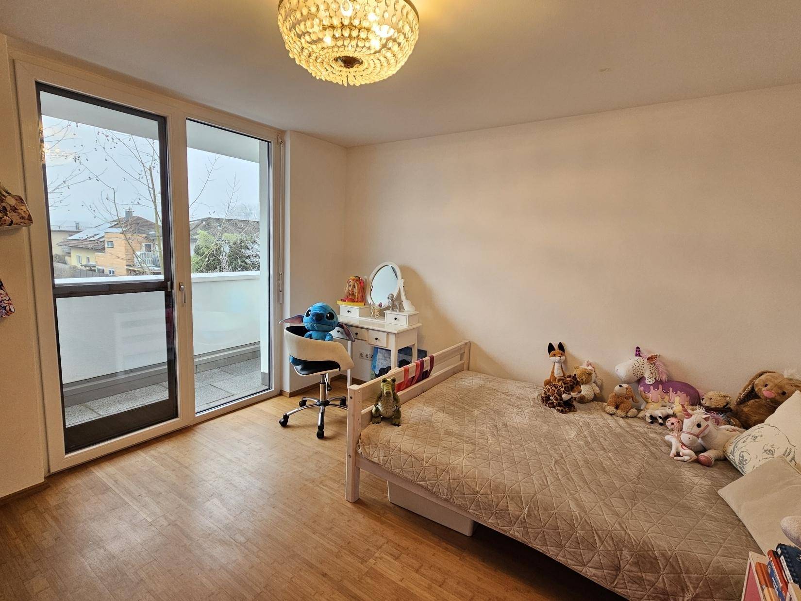 Helles Kinderzimmer mit Holzboden, Bett und Zugang zu einem kleinen Balkon.