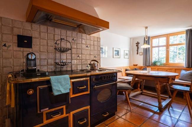 Traditionelle Küche mit Holzofen, Fliesenboden und gemütlicher Essecke am Fenster.