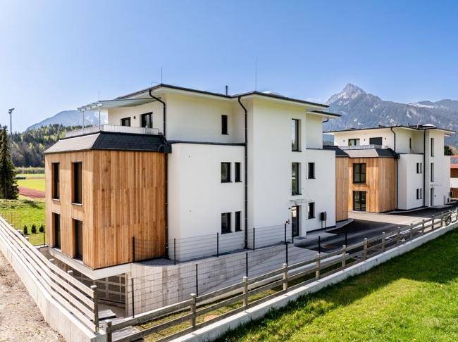 Moderne Wohnanlage mit Holzfassade und Zugang zur Tiefgarage, umgeben von Natur.