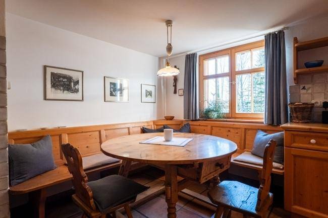 Gemütliche Essecke in der Küche mit Holzbänken, rundem Tisch und Blick ins Grüne.