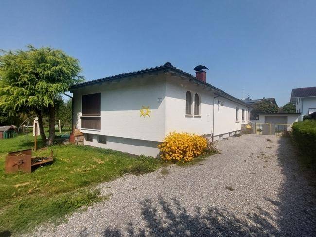 Seitenansicht des Hauses mit Kiesauffahrt und blühenden Sträuchern unter blauem Himmel.