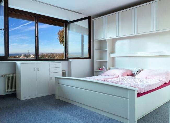 Schlafzimmer mit Einbauschränken, Teppichboden und weitem Blick auf die Landschaft.