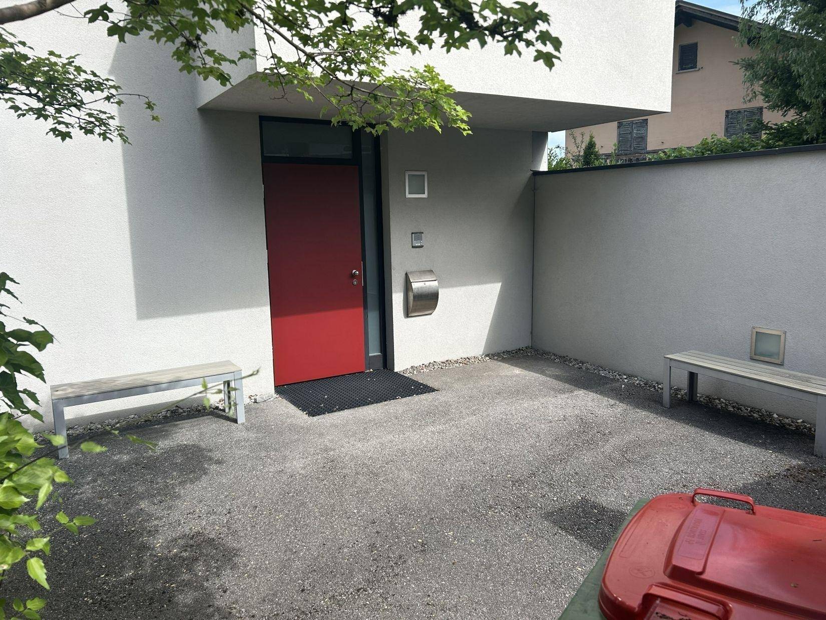 Eingangsbereich des Hauses mit roter Tür, zwei Bänken und einem modernen Briefkasten.