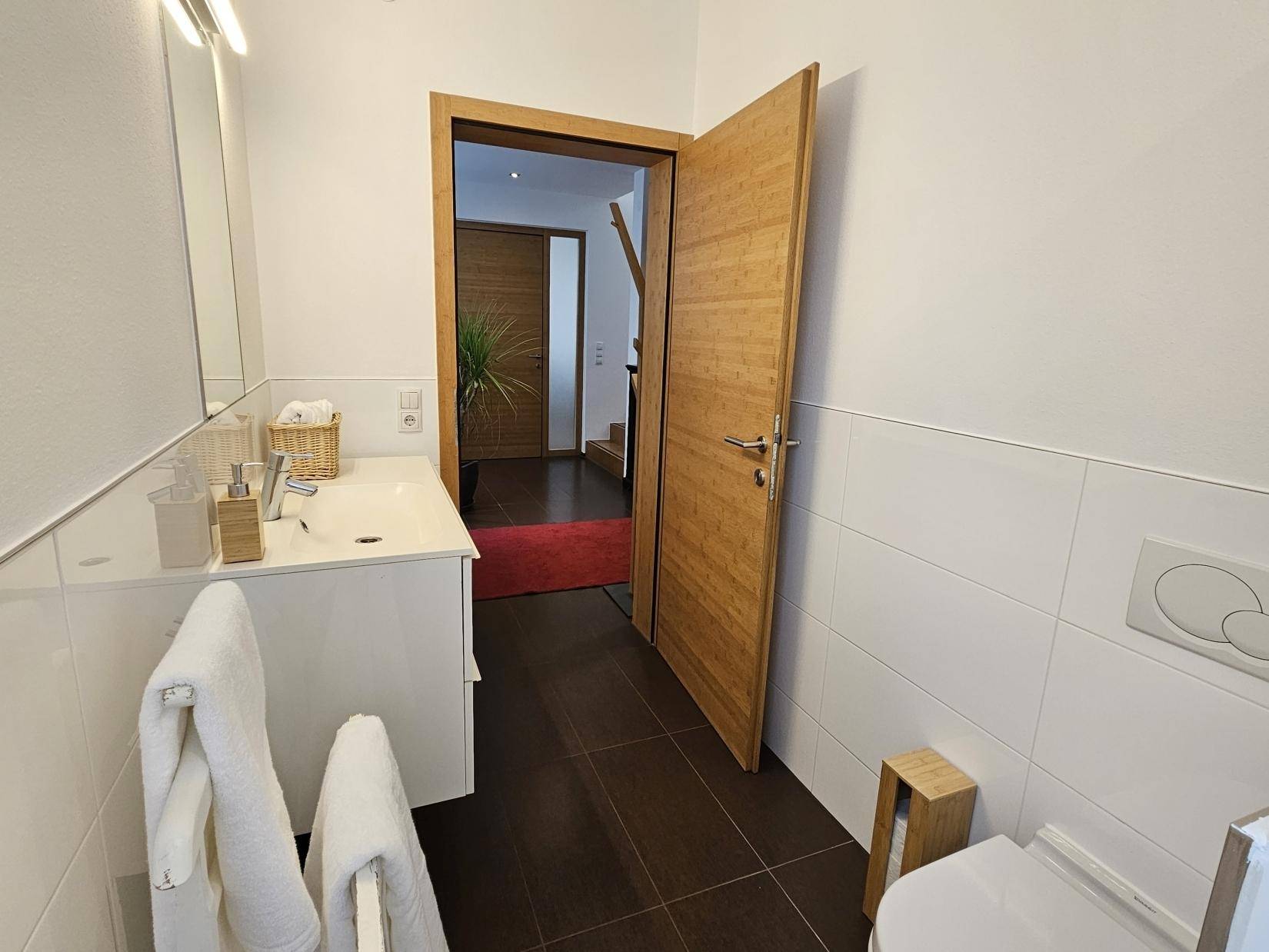 Badezimmer mit Waschtisch und Blick in den Flur mit Holzdetails.