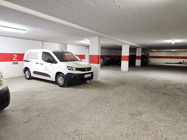 Geräumige Tiefgarage mit mehreren Stellplätzen, beleuchtet und mit weiß-roten Markierungen an den Wänden.