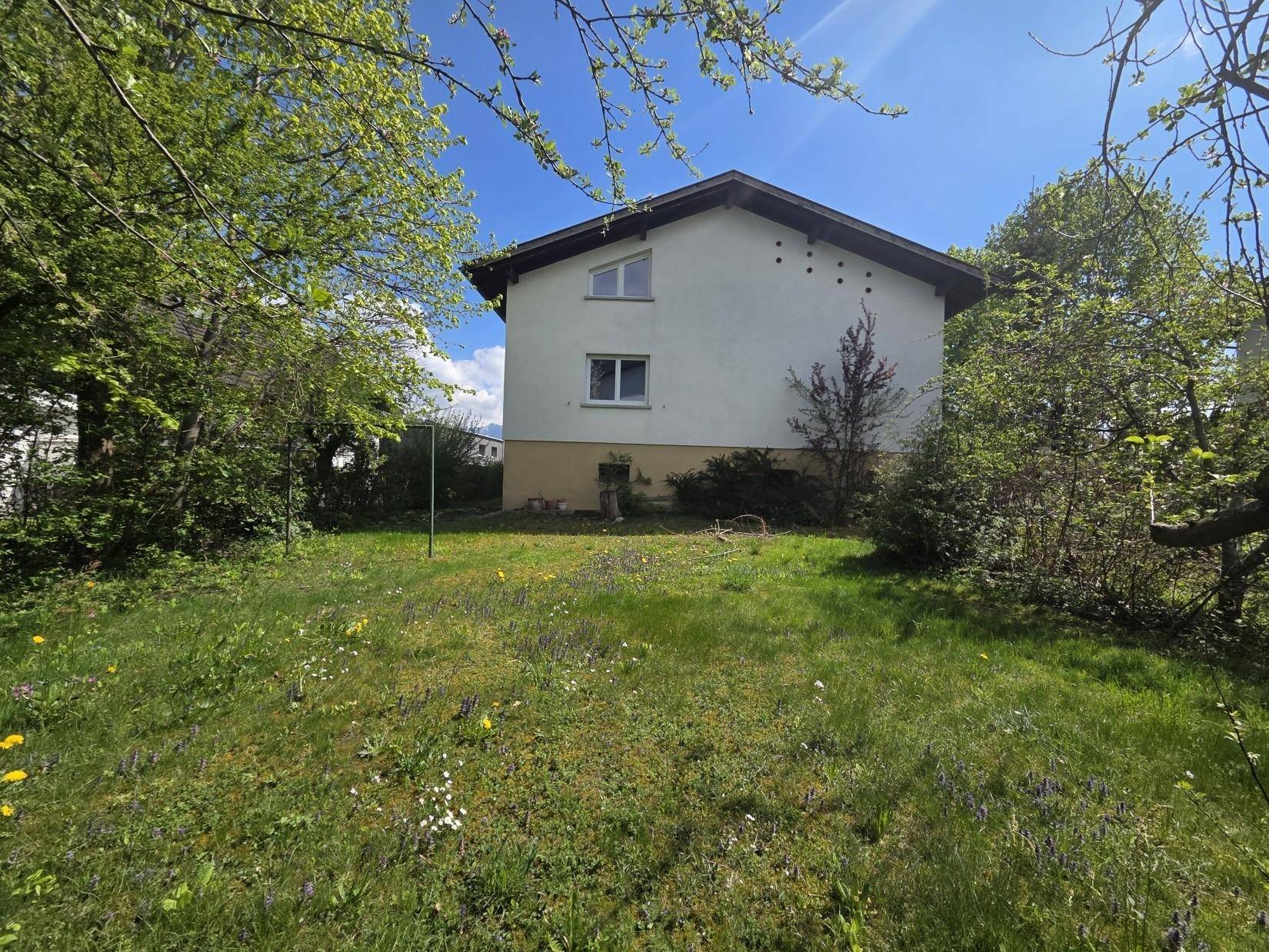 Ansicht des Hauses von der Gartenseite mit grüner Umgebung und blauem Himmel.