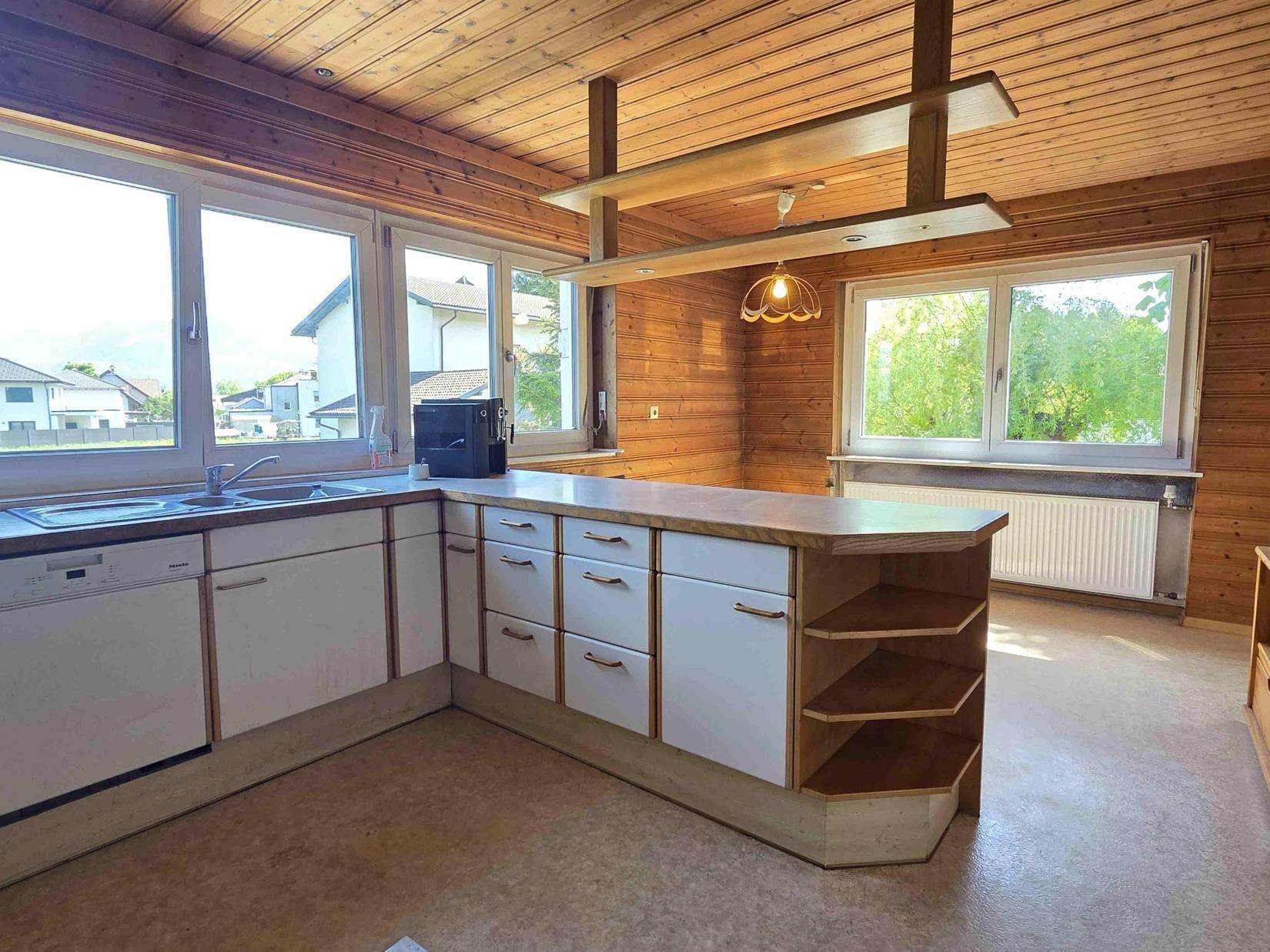 Geräumige Küche mit Holzdecke, integrierter Kücheninsel und großzügigen Fenstern.