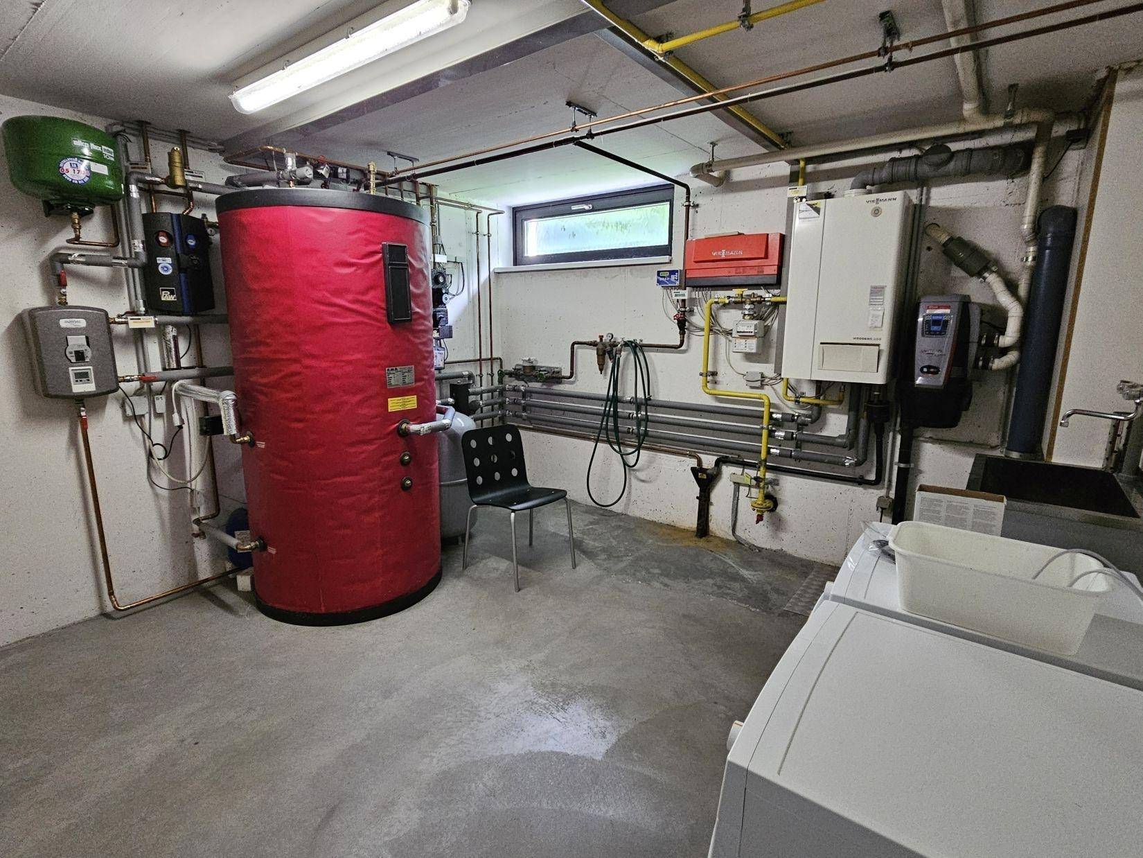 Technikraum mit Warmwasserspeicher, Heizungsanlagen und Anschlüssen für Waschmaschine.