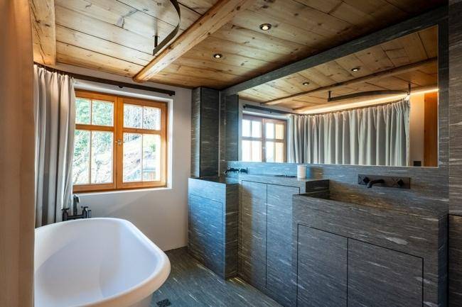 Modernes Badezimmer mit freistehender Badewanne, Doppelwaschbecken und dunklen Steinfliesen, die Eleganz verleihen.
