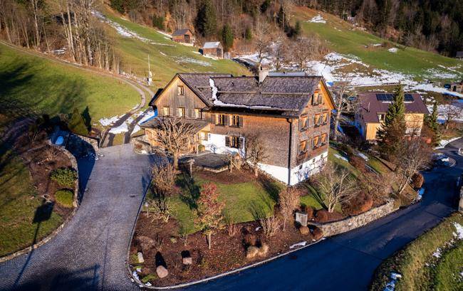 Vogelperspektive des Anwesens mit dem Holzhaus, umgeben von gepflegten Gärten und Zufahrtswegen.