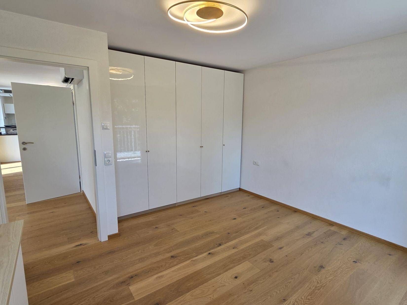 Schlafzimmer mit hellem Eichenparkett und einer modernen, glänzenden Schrankwand.