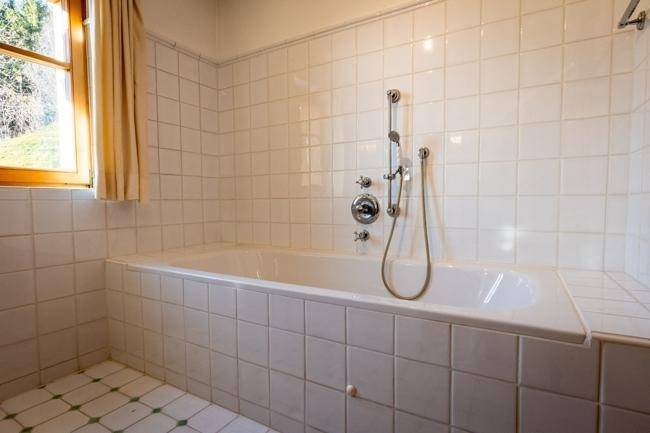 Klassisches Badezimmer mit weiß gefliester Badewanne und Duscharmatur, sowie einem Fenster für Tageslicht.