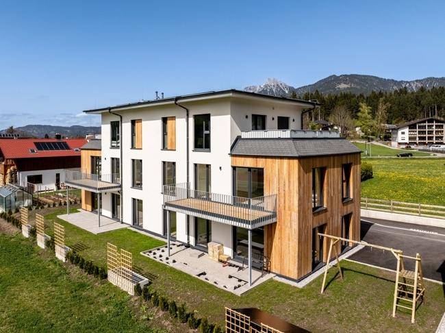 Seitenansicht des modernen Gebäudes mit Holzverkleidung, Balkonen und Blick auf die Berge.