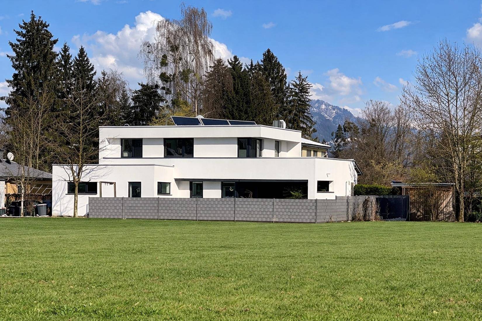 Modernes Wohnhaus mit Flachdach und Solaranlage, umgeben von grüner Landschaft.
