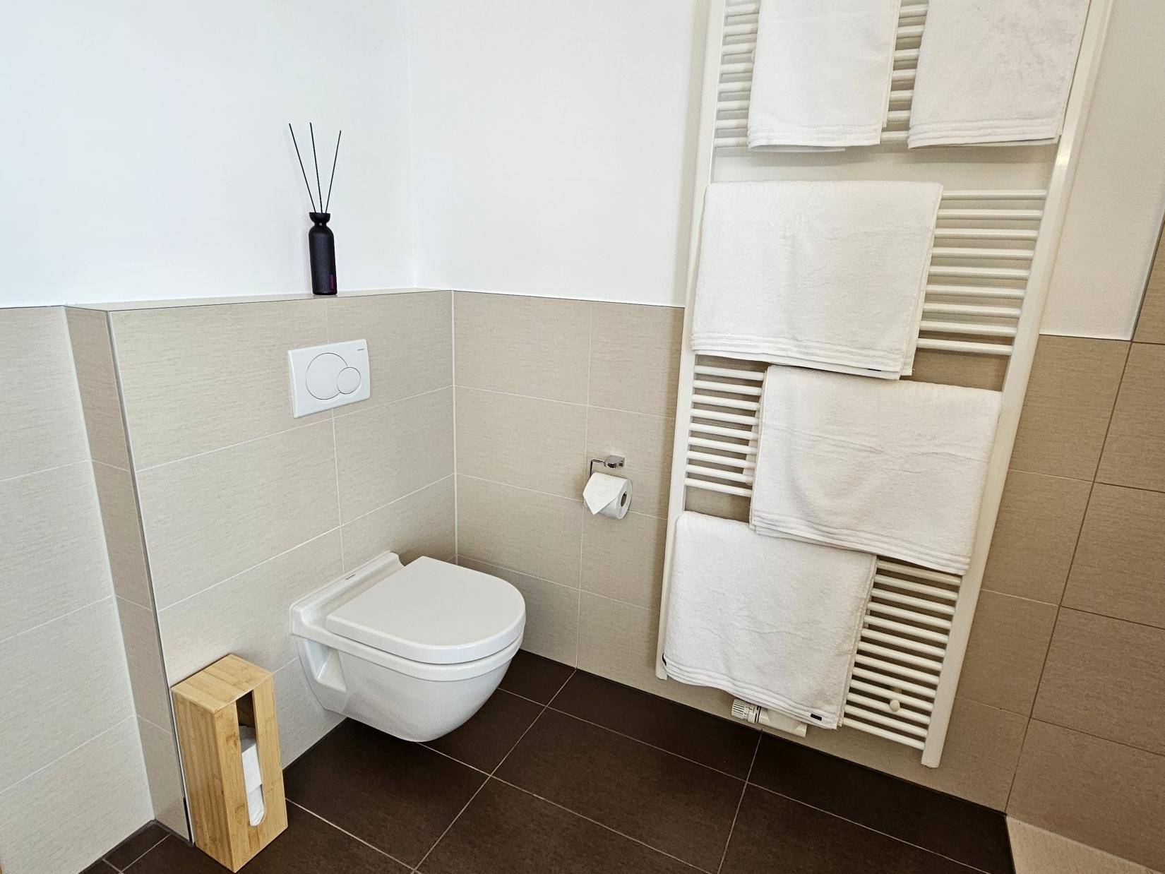 Modernes WC mit Wandtoilette und beheiztem Handtuchhalter.