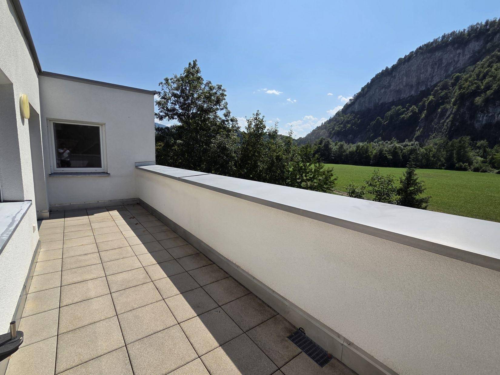 Sonniger Terrassenbereich mit Fliesenboden und freiem Blick auf die grüne Berglandschaft.
