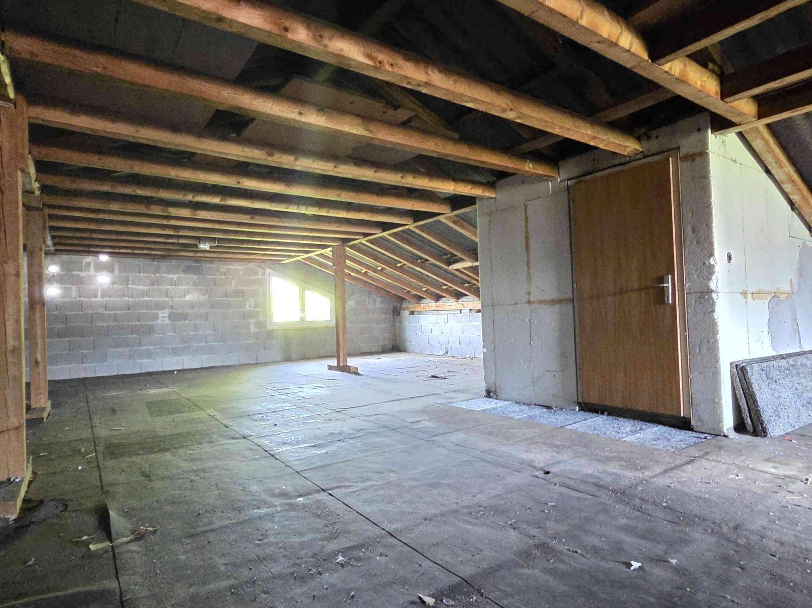 Dachboden mit Holzbalken, Fenster und Tür, bietet viel ungenutzten Raum.