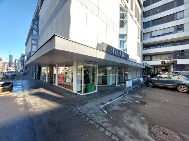 Ansicht der Geschäftsfassade mit großen Schaufenstern und angrenzendem Parkplatzbereich.