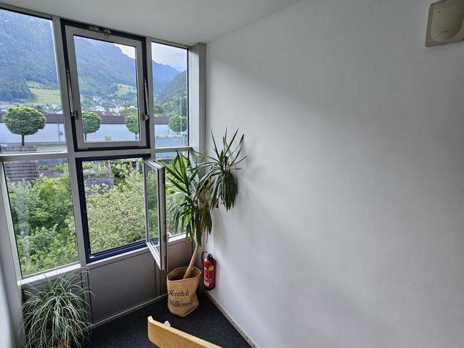 Treppenhaus mit großen Fenstern, die einen weiten Blick auf die grüne Umgebung und Berge bieten.