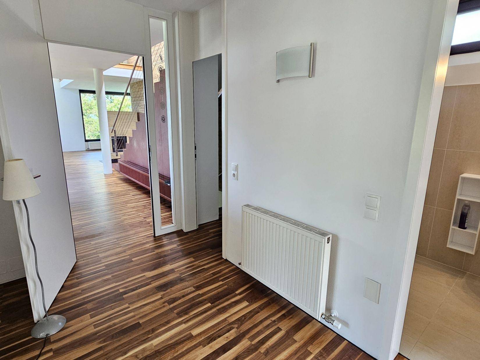 Heller Flur mit Holzparkettboden, Heizkörper und Blick in den offenen Wohnbereich.