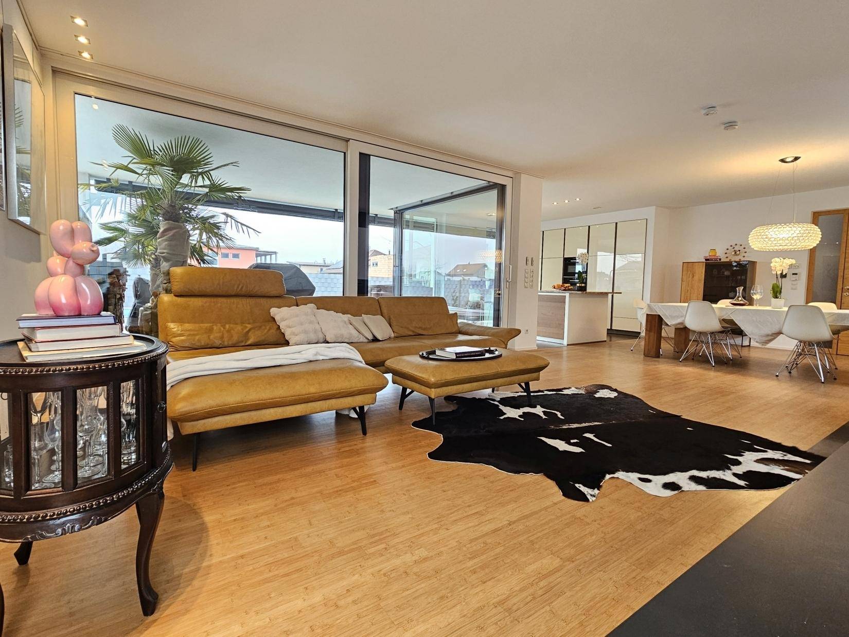 Offener Wohnbereich mit Ledersofa, Holzboden und Blick auf den Essbereich und die Küche.