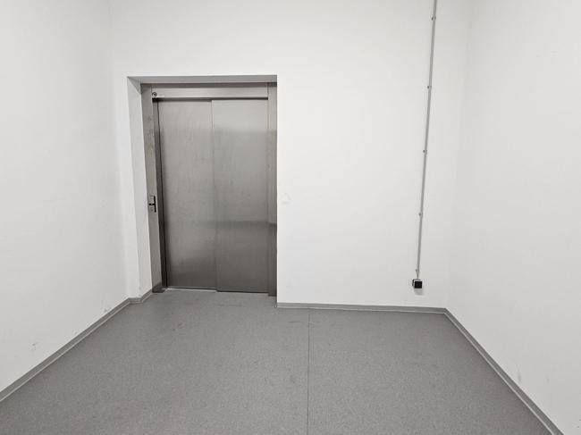 Heller Flur mit einem modernen Aufzug und schlichtem Bodenbelag in einem Geschäftsgebäude.