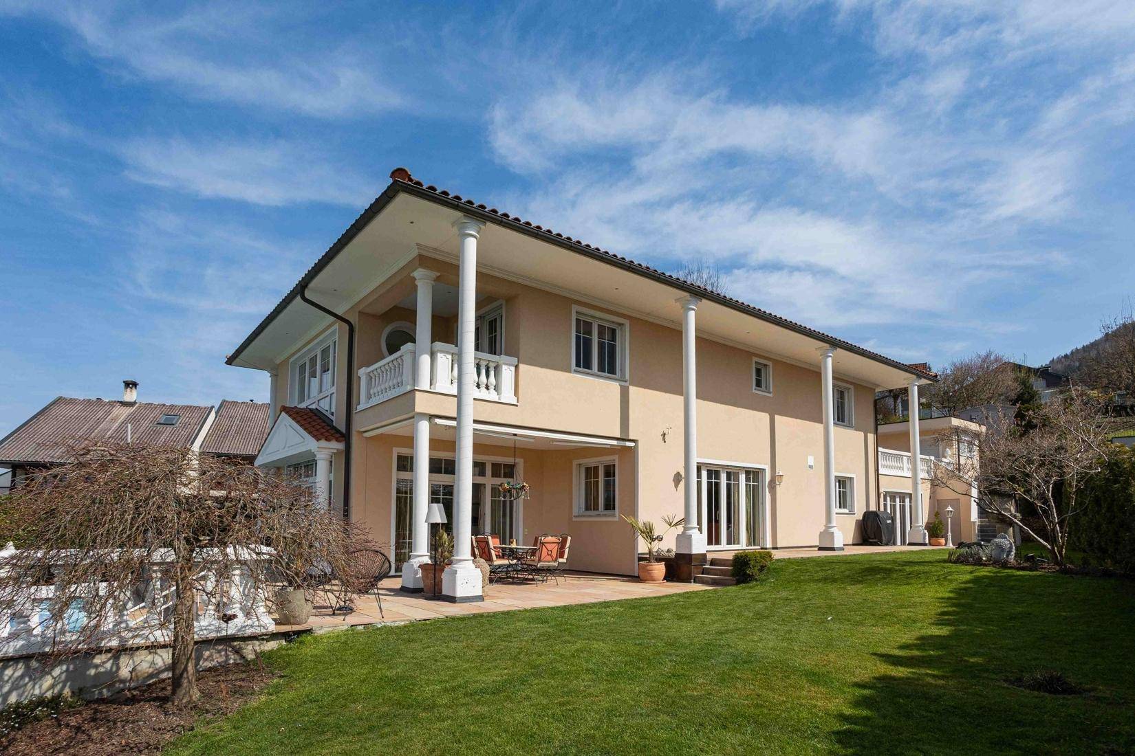 Rückansicht der Villa mit weitläufigem Rasen, Terrasse und klassischer Architektur.